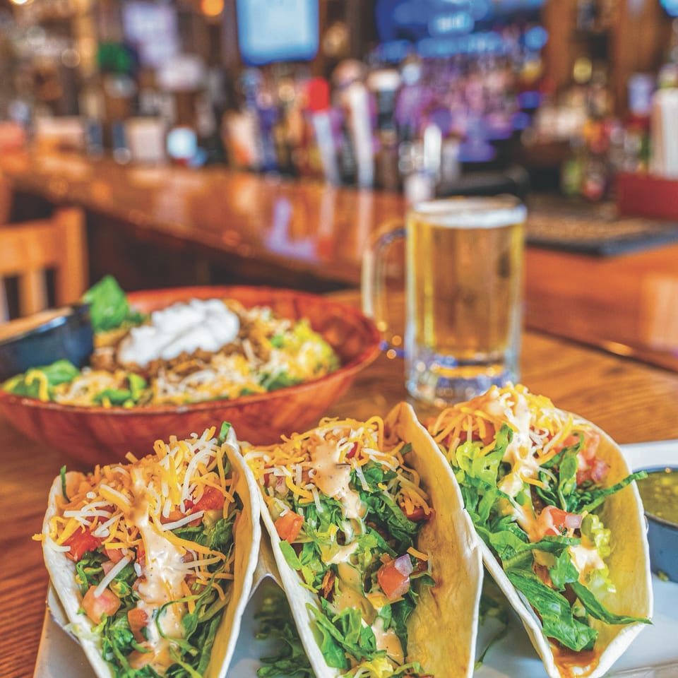 Three tacos with a beer at the bar.