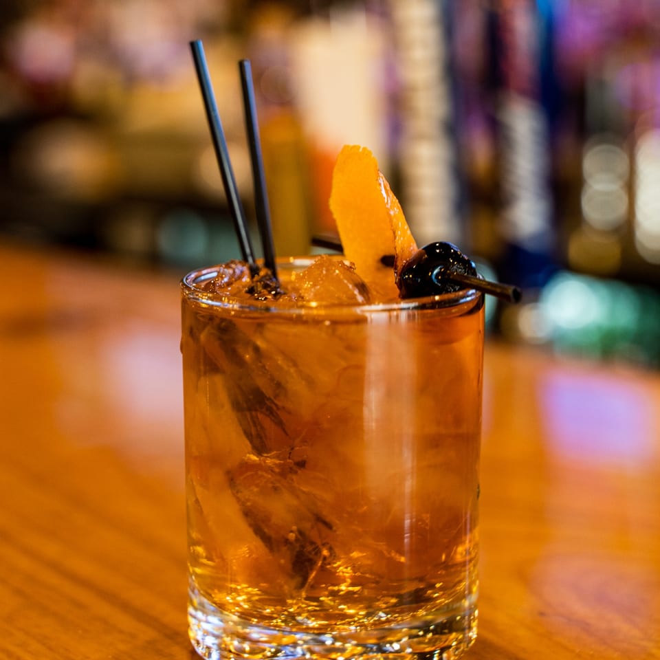 Whiskey cocktail with orange peel and cherry.