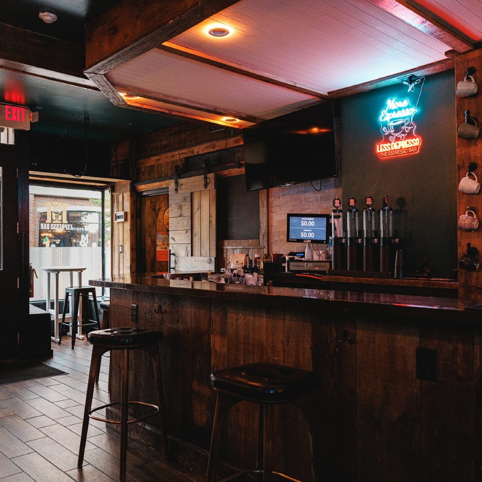 Espresso Bar interior with wood counter, stools, and neon sign.