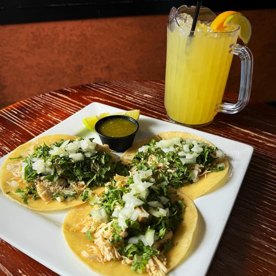 Chicken tacos with onions, cilantro, salsa, and a citrus drink.