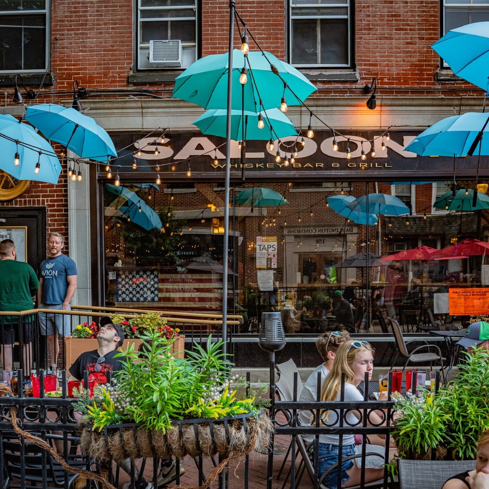 Saloon 151 storefront with blue umbrellas and patio seating.
